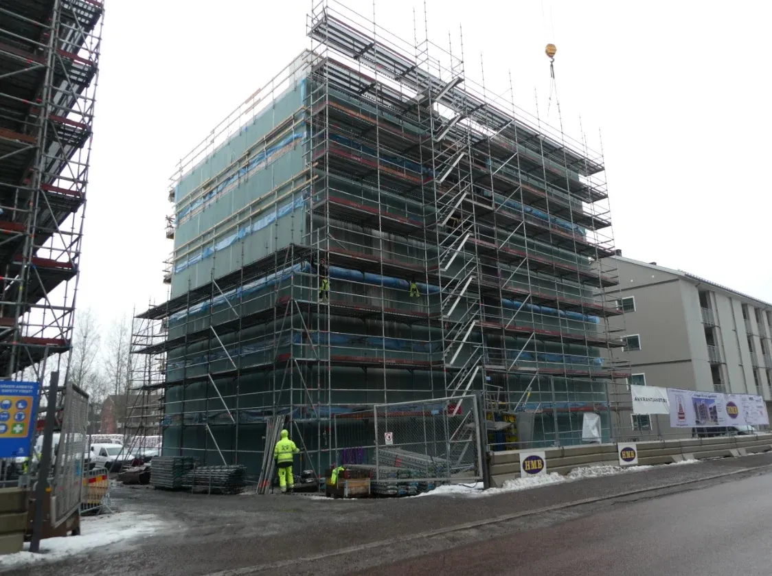 Fasad inklädd i byggnadsställning med montörer i arbete.