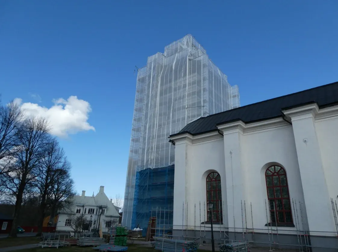 Kyrkan och det inklädda tornet frontalt i solsken.