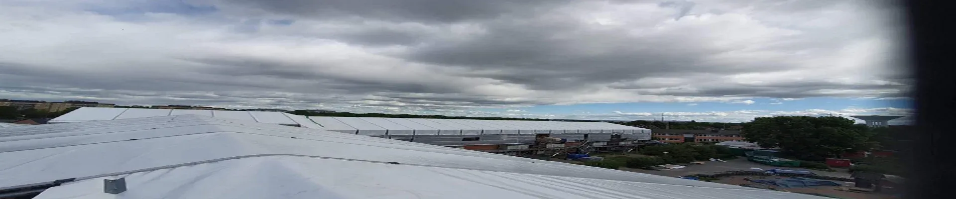 Vy över ett stort väderskyddstak med industriområde i bakgrunden.